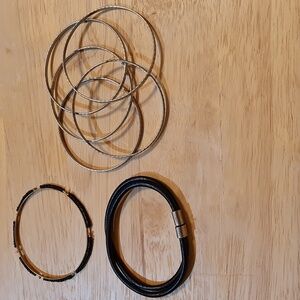 Set of 7 bracelets. 5 are silver tone hammered metal, 1 leather like, 1 black